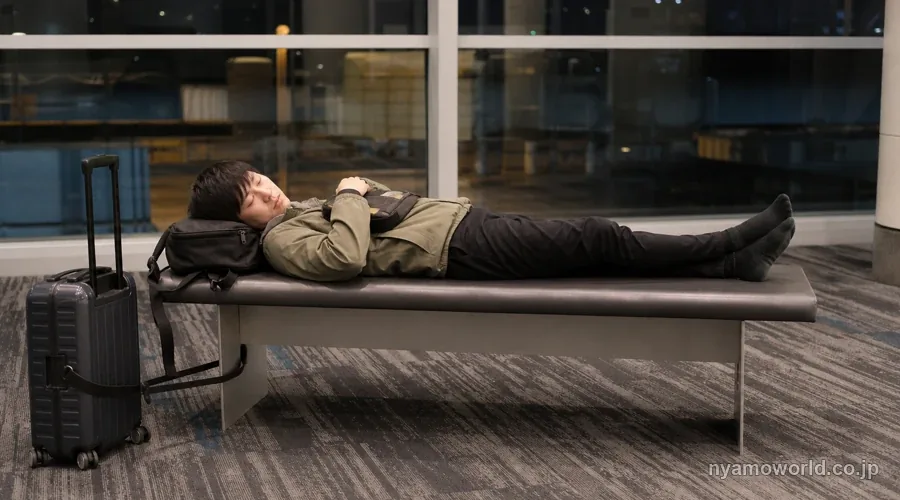 空港のベンチで荷物を抱えて仮眠する日本人旅行者