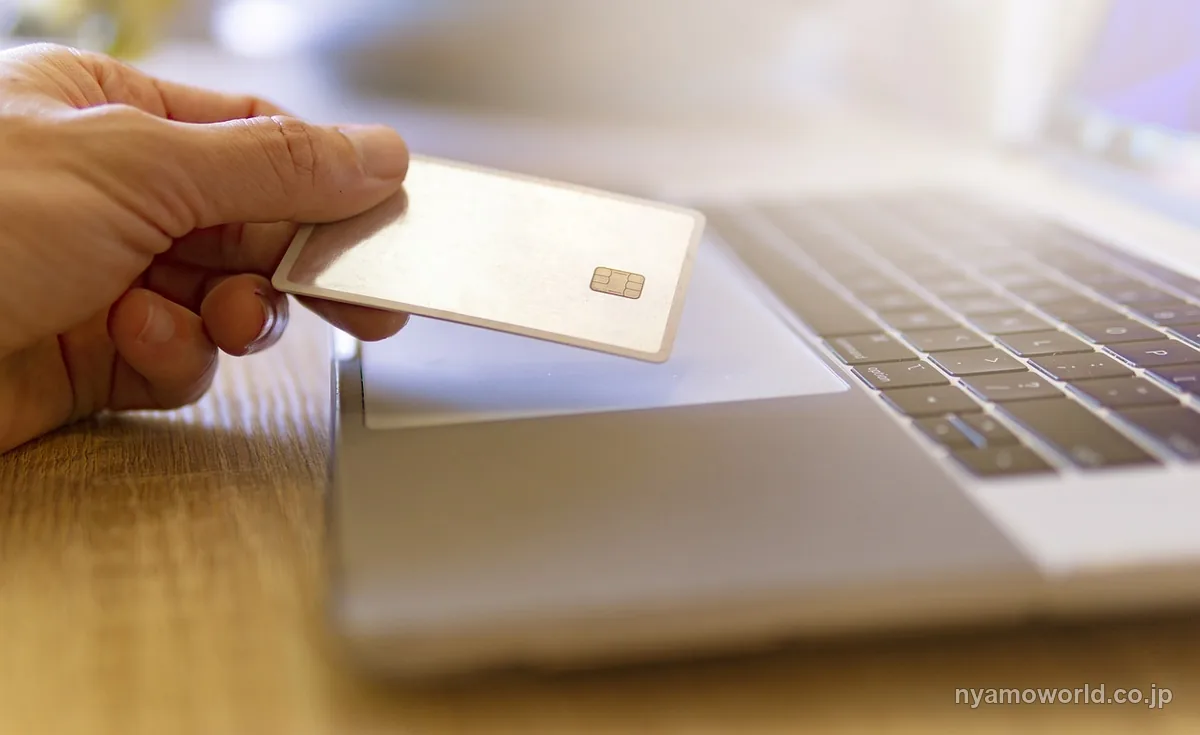 ノートパソコンの前でクレジットカードを手にしている、日常のカード決済のイメージ
